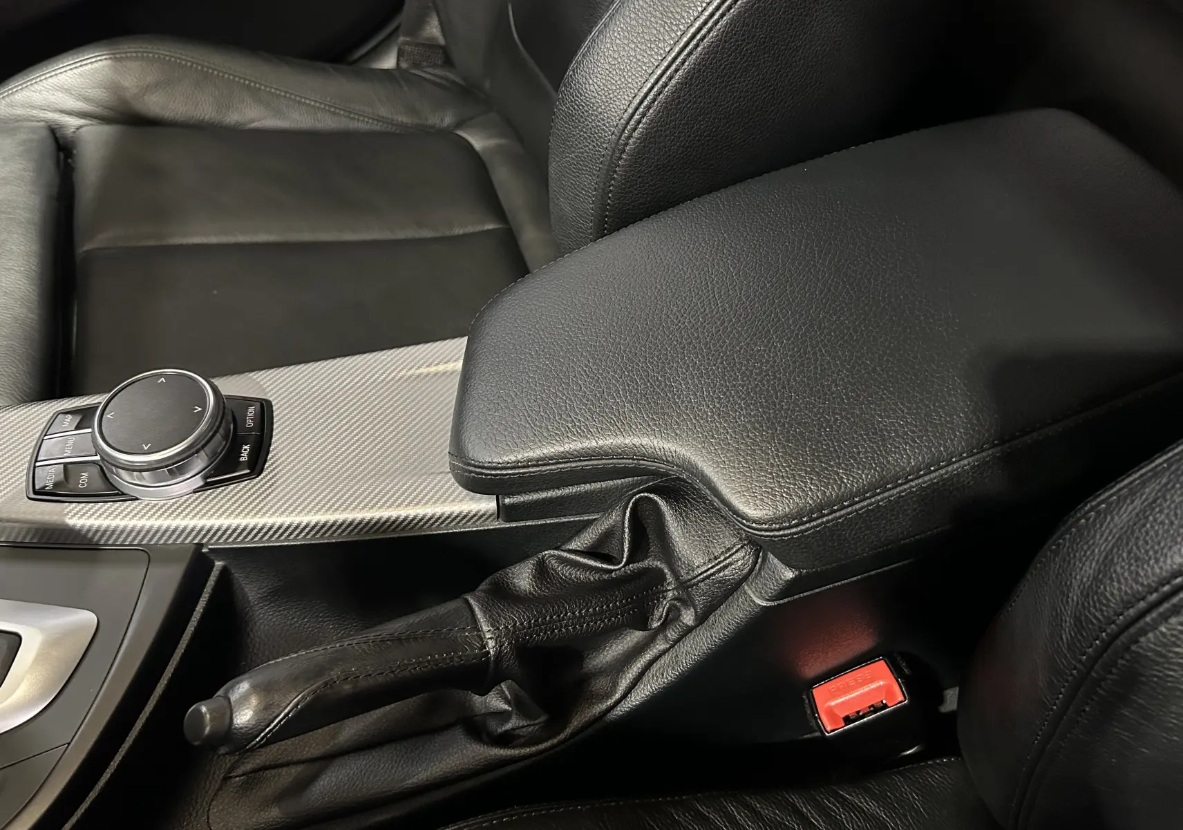 Gros plan intérieur sur la console centrale en cuir noir avec frein à main et commande iDrive d'une BMW Série 3 blanche 320i 2018.