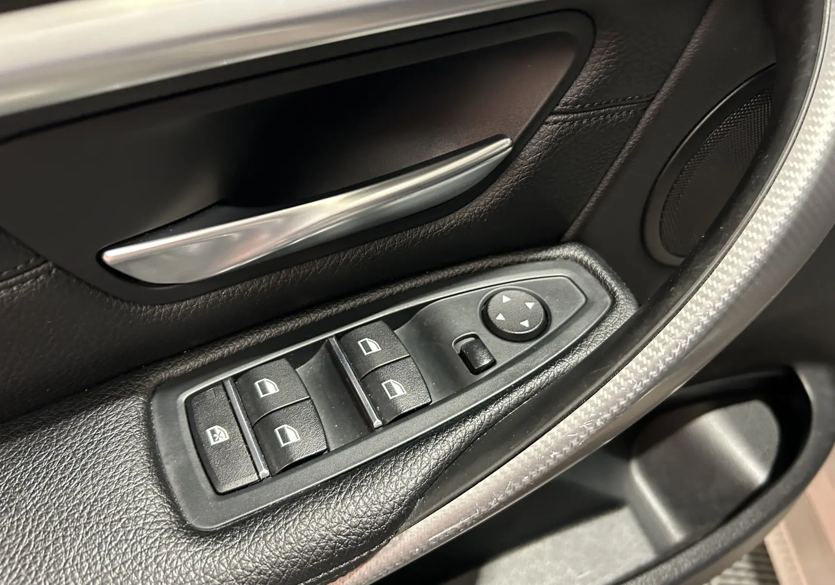 Gros plan sur les commandes de lève-vitres et rétroviseurs côté conducteur d'une BMW Série 3 blanche 320i 2018.