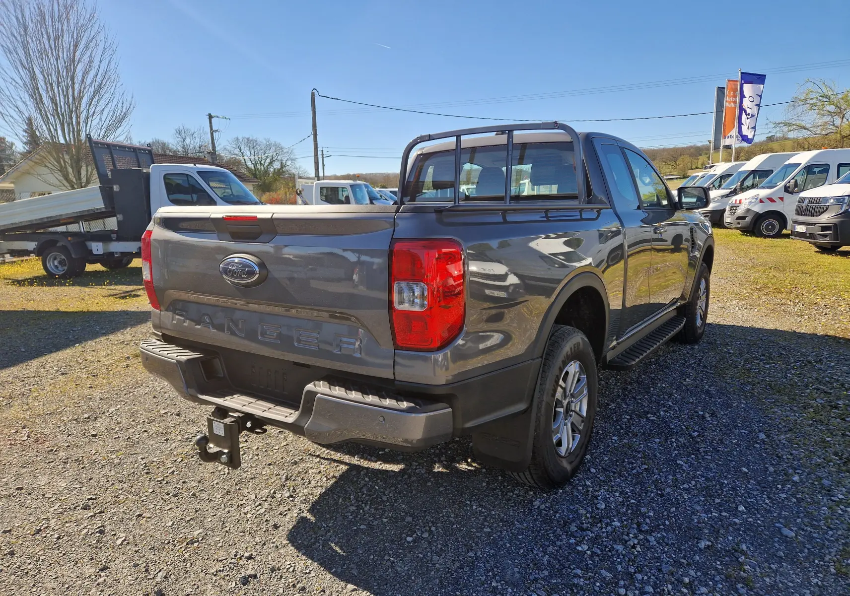 Vue 3/4 arrière droite d'un Ford Ranger Super Cabine gris carbone avec attelage et barres de protection sur la benne.