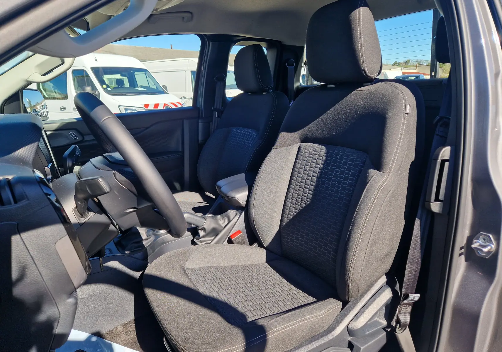 Vue intérieure côté conducteur du Ford Ranger Super Cabine gris carbone 2026, mettant en valeur les sièges avant en tissu et le volant multifonction.