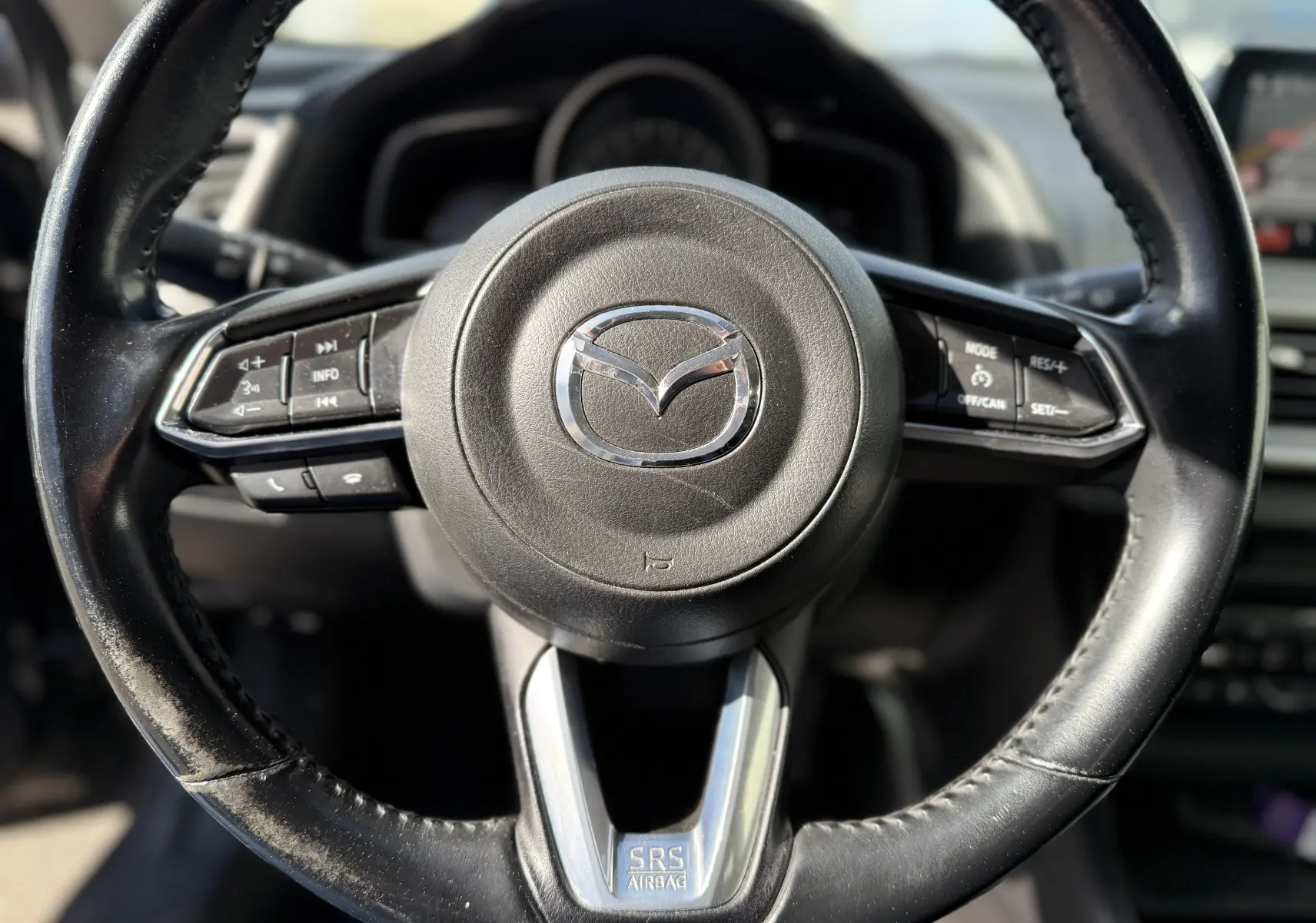 Gros plan sur le volant noir en cuir de la Mazda3 2017, avec commandes intégrées et logo Mazda central chromé.