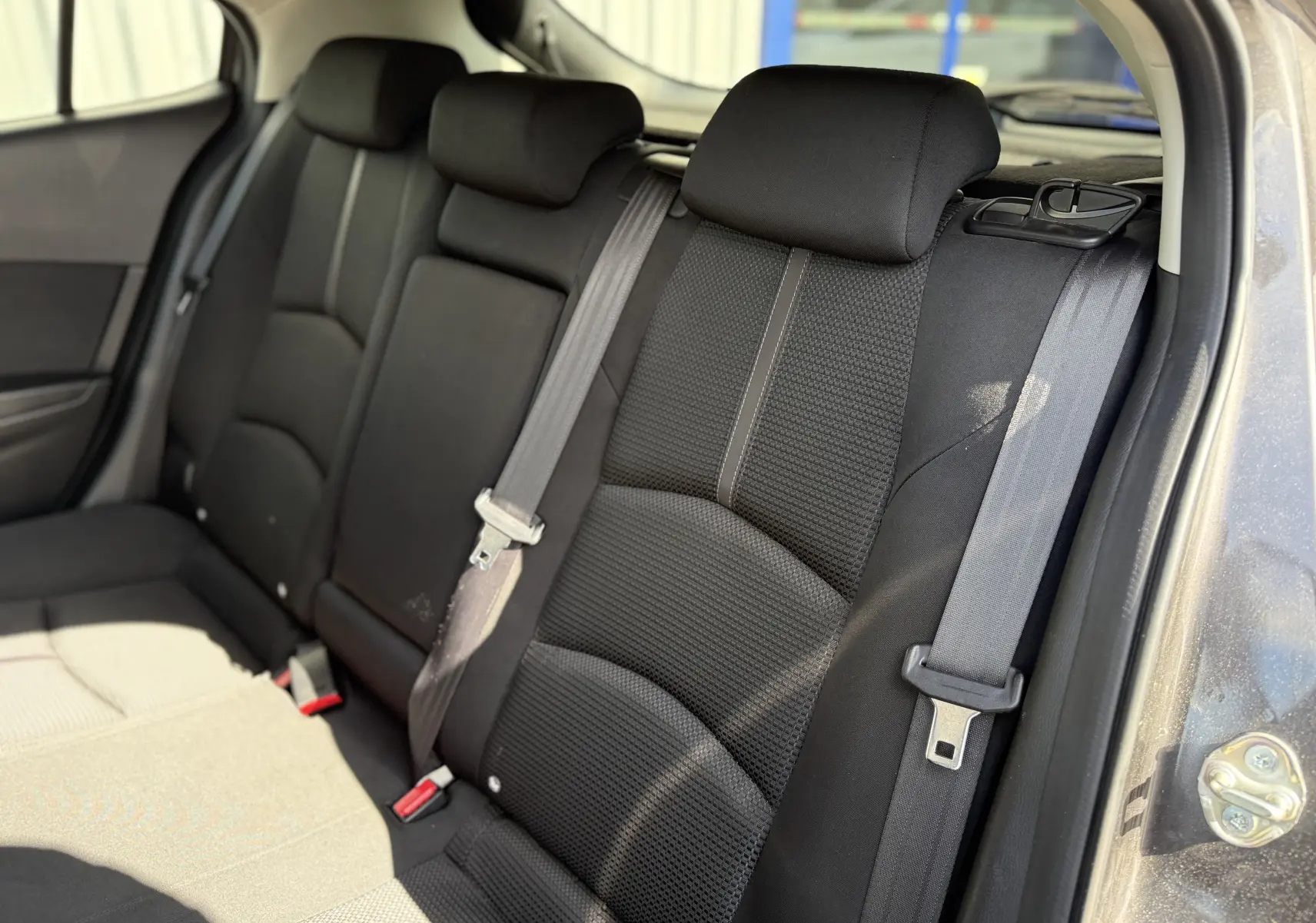 Vue intérieure sur les sièges arrière en tissu noir de la Mazda3 gris 2017, avec ceintures de sécurité visibles.