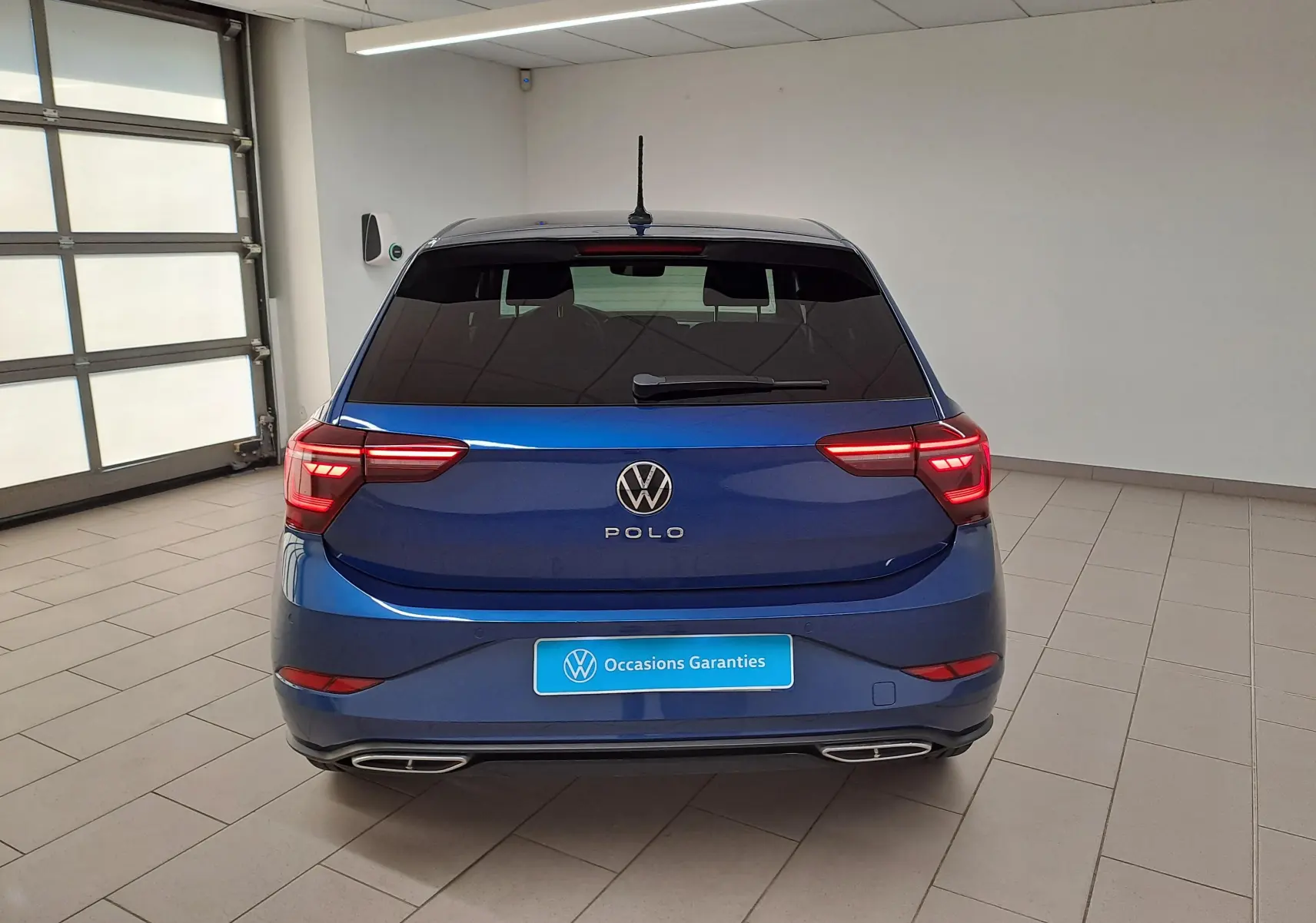 Vue arrière d'une Volkswagen Polo Bleu Récif avec feux allumés et double sortie d'échappement intégrée au pare-chocs.