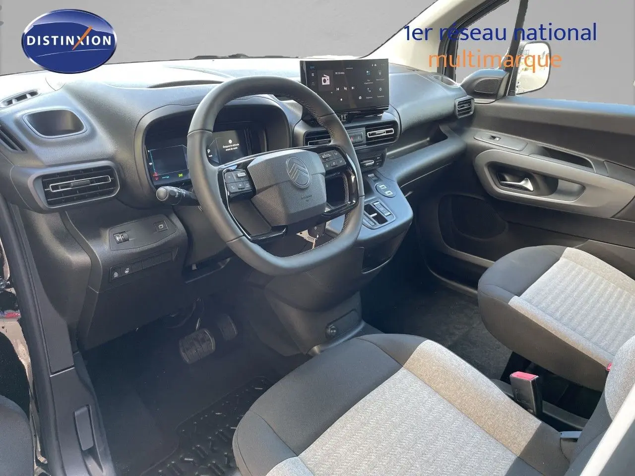 Vue intérieure côté conducteur du Citroën Berlingo 2026, tableau de bord noir avec volant multifonction et sièges tissu bicolore.
