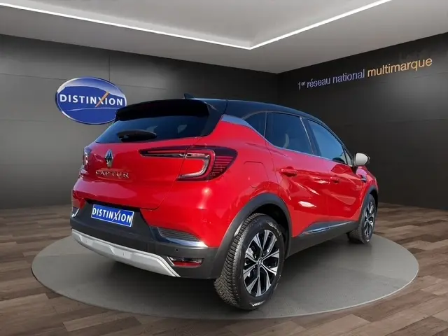 Vue 3/4 arrière droite d'un Renault Captur Techno TCe 90 rouge brillant avec toit noir et jantes alliage bicolores.