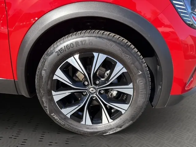Gros plan sur la roue avant droite du Renault Captur rouge 2024 avec jante alliage bicolore et logo central Renault.