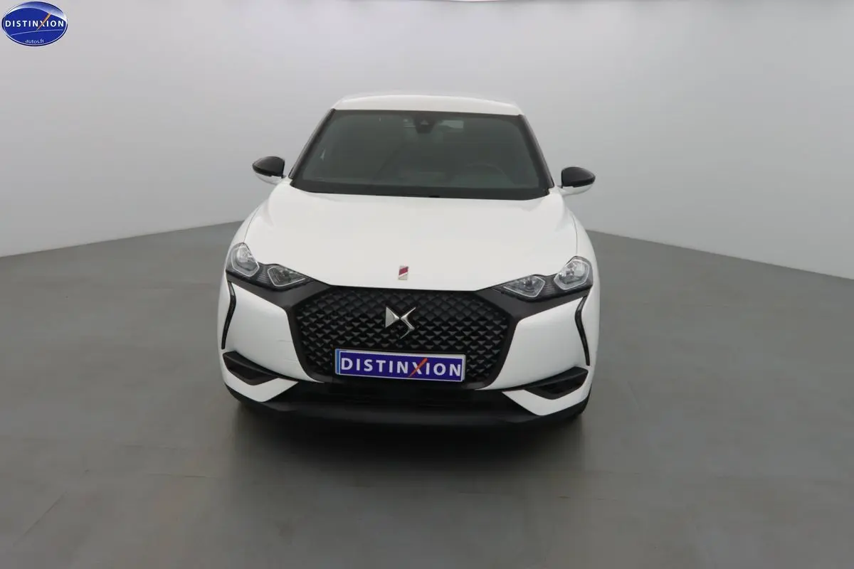 Vue frontale d'une DS3 Crossback blanc banquise avec calandre noire et phares anguleux dans un studio gris.
