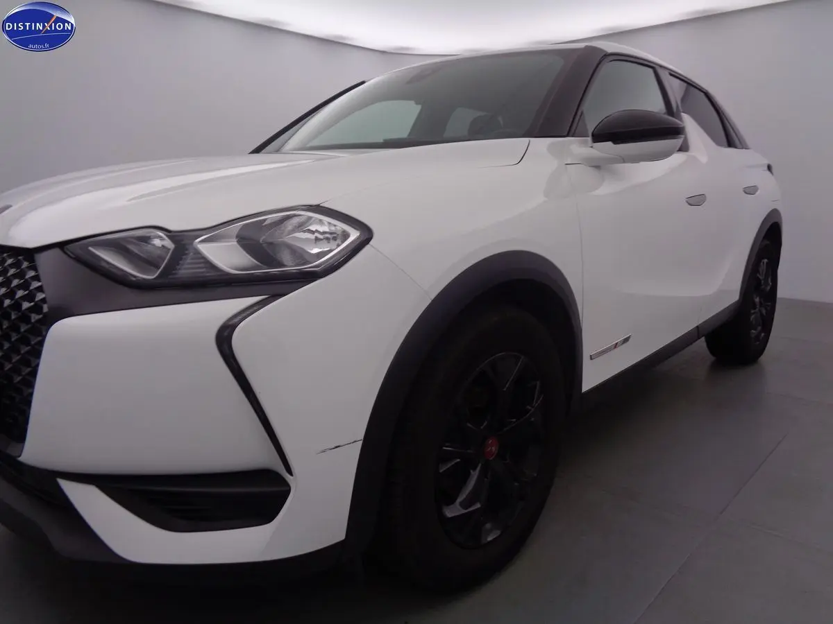 Vue 3/4 avant droit d'un DS3 Crossback blanc banquise avec jantes noires et calandre distinctive en losange.