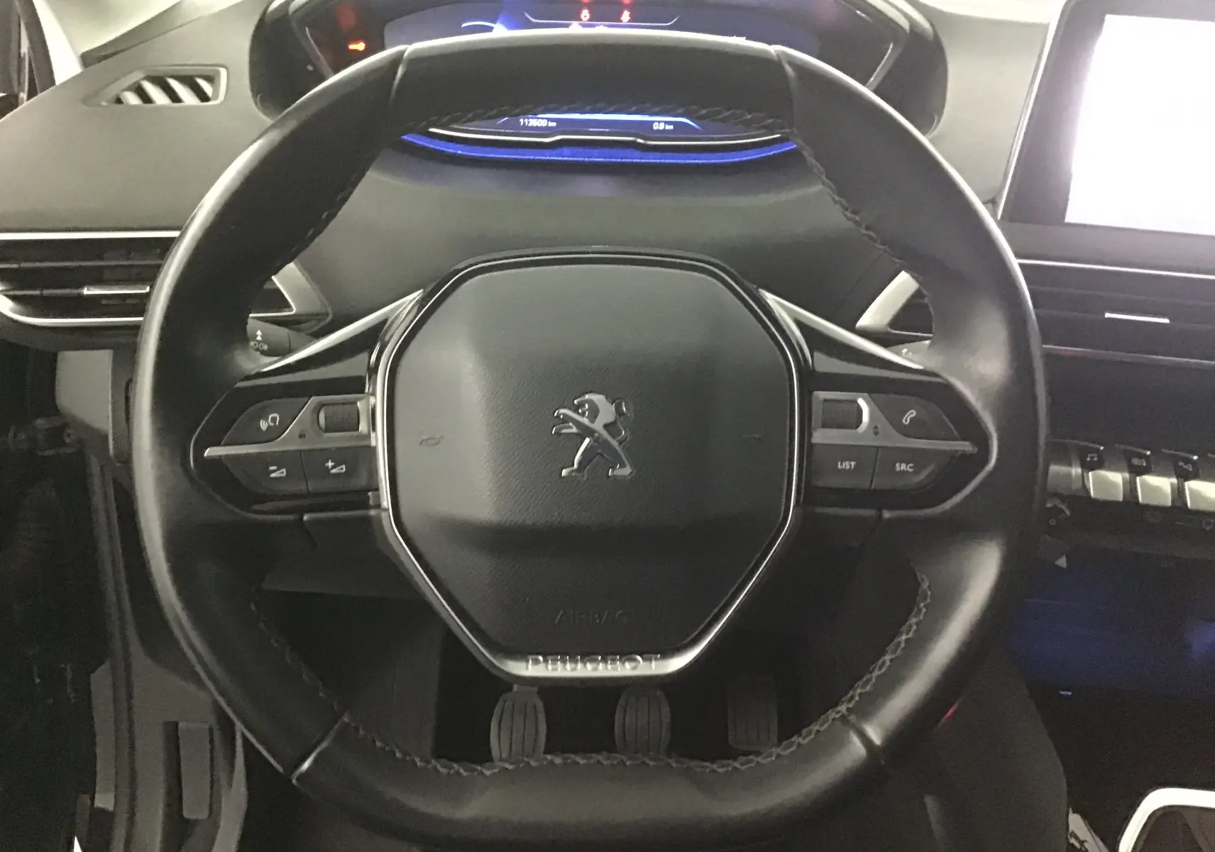 Vue rapprochée du volant cuir noir du Peugeot 5008 2019 avec commandes intégrées et tableau de bord digital bleu.