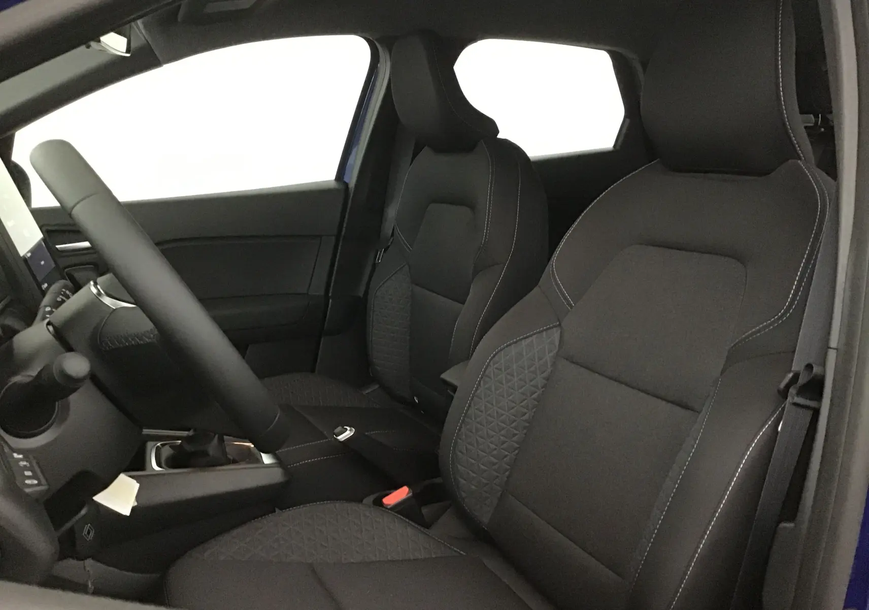 Vue intérieure côté conducteur du Renault Captur 2025 bleu iron/noir, sièges avant en tissu noir avec surpiqûres blanches.