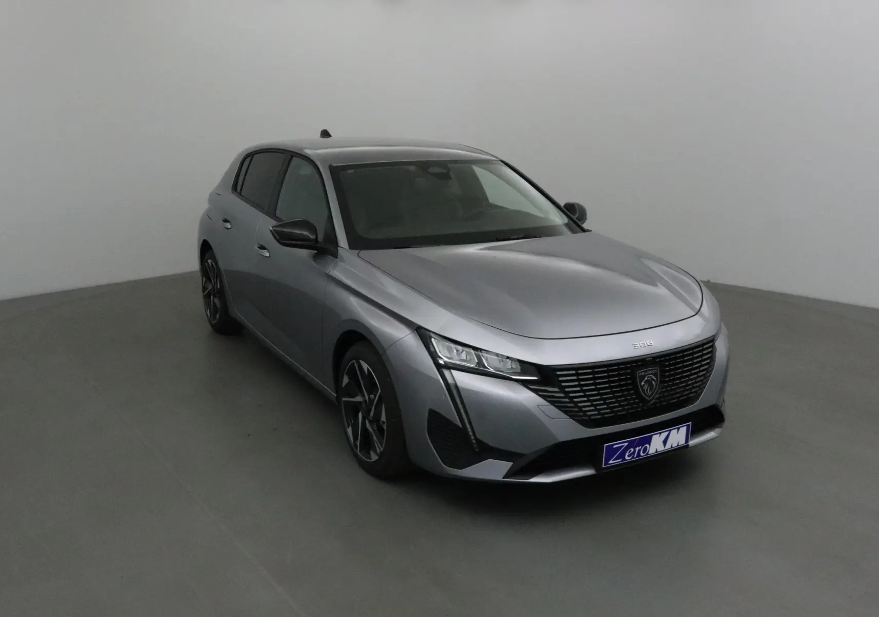 Peugeot 308 gris Artense vue 3/4 avant droit, avec calandre noire et jantes alliage distinctives.