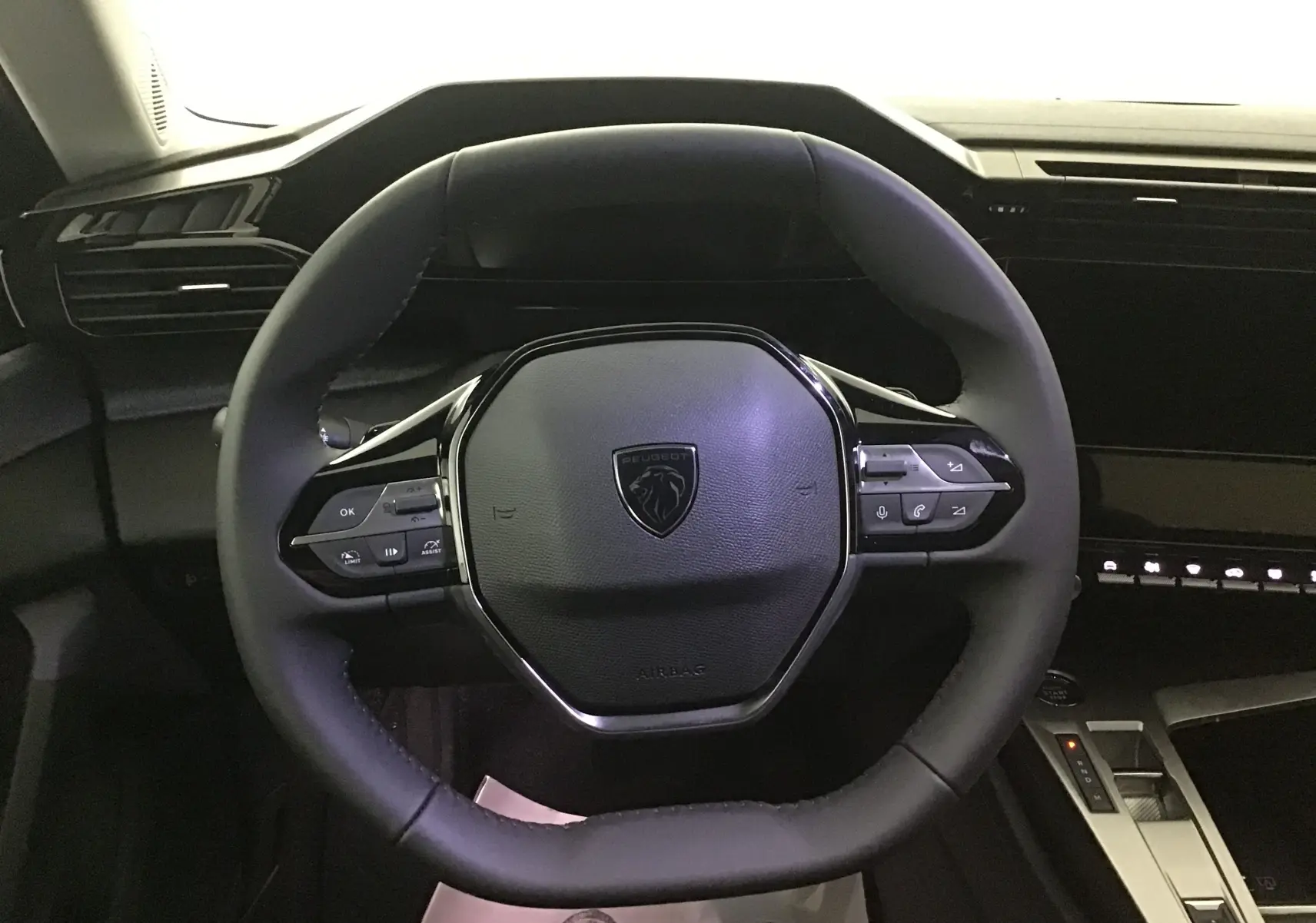 Vue rapprochée du volant cuir noir du Peugeot 308 gris Artense, avec commandes intégrées et tableau de bord moderne.