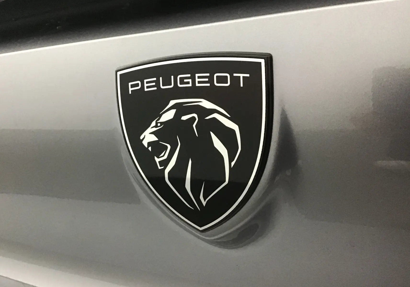 Gros plan sur l'emblème Peugeot noir et blanc sur la carrosserie gris artense d'une 308 diesel.