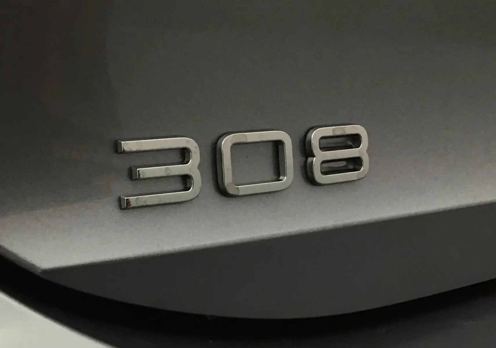 Gros plan sur l’inscription 308 en chrome sur la carrosserie gris artense d’une Peugeot 308.