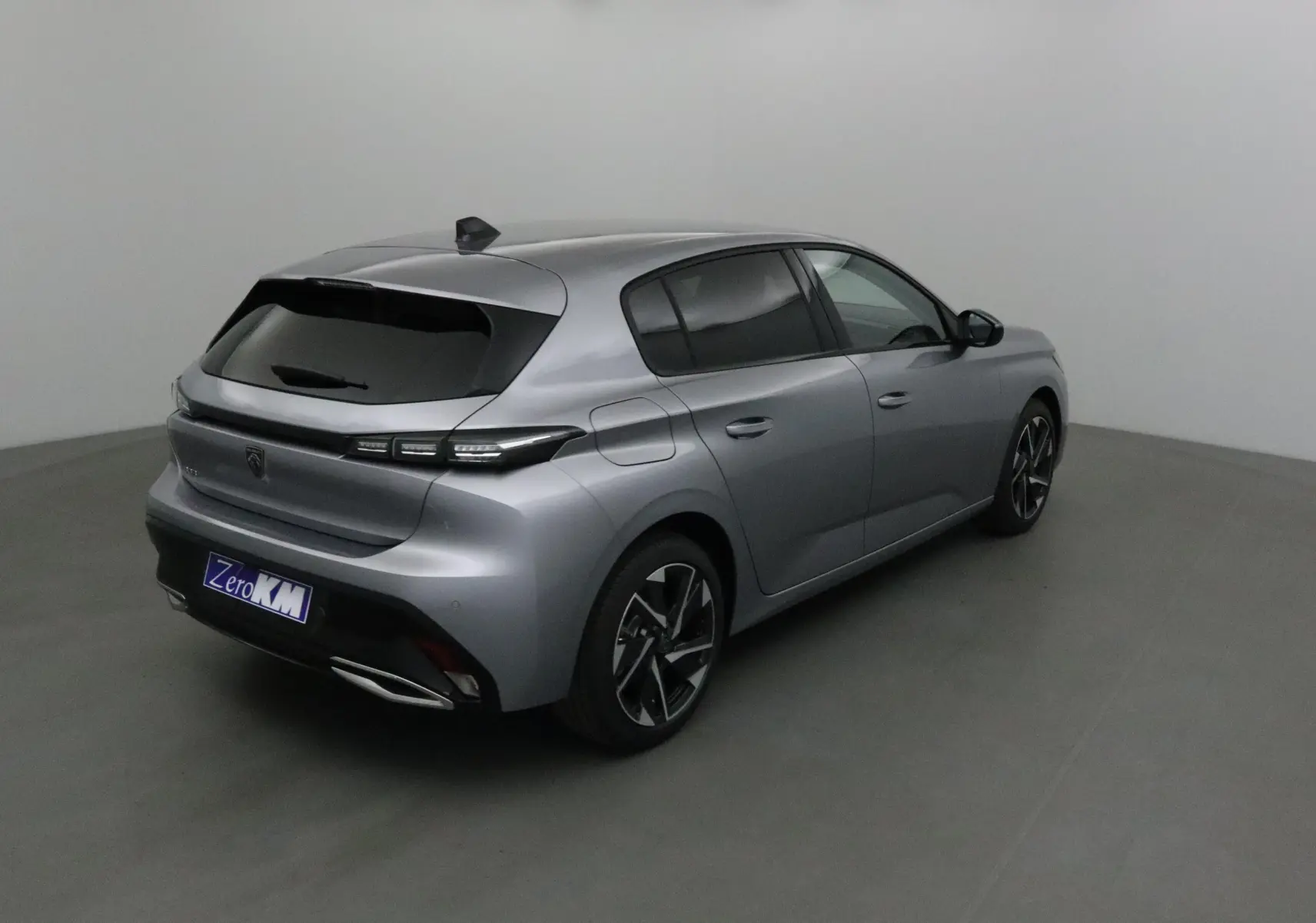 Peugeot 308 gris Artense vue 3/4 arrière droit dans un studio, avec vitres teintées et jantes alliage noires.