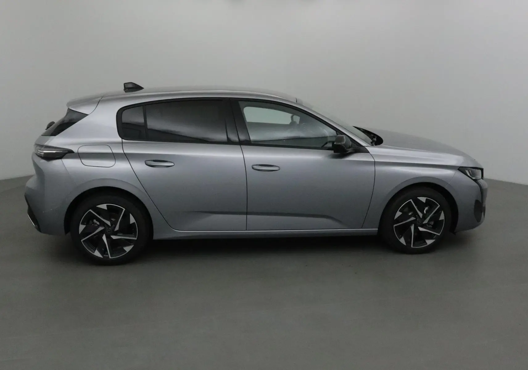 Profil côté droit de la Peugeot 308 gris Artense avec jantes alliage noires et vitres teintées sur fond neutre.