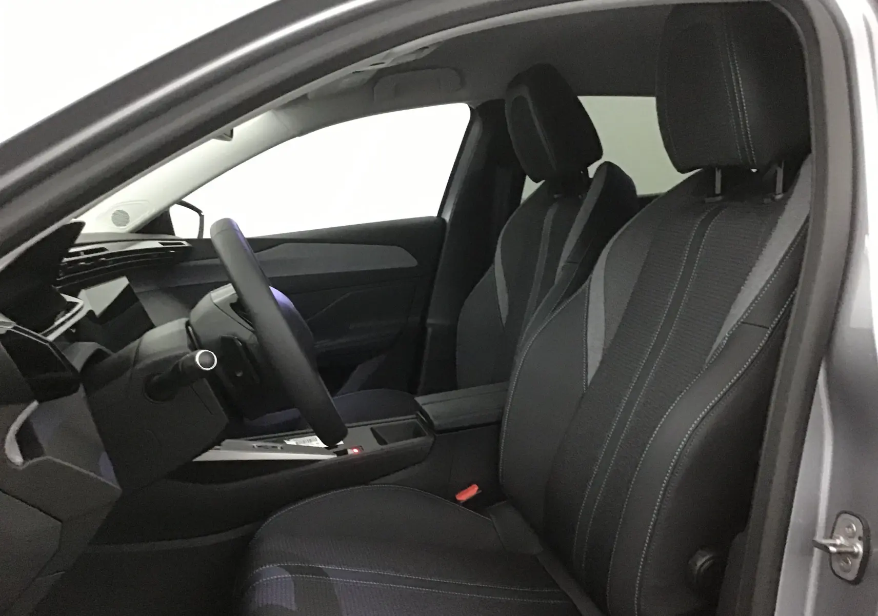 Intérieur de la Peugeot 308 gris Artense, vue côté conducteur, sièges en tissu avec surpiqûres contrastées et volant cuir.