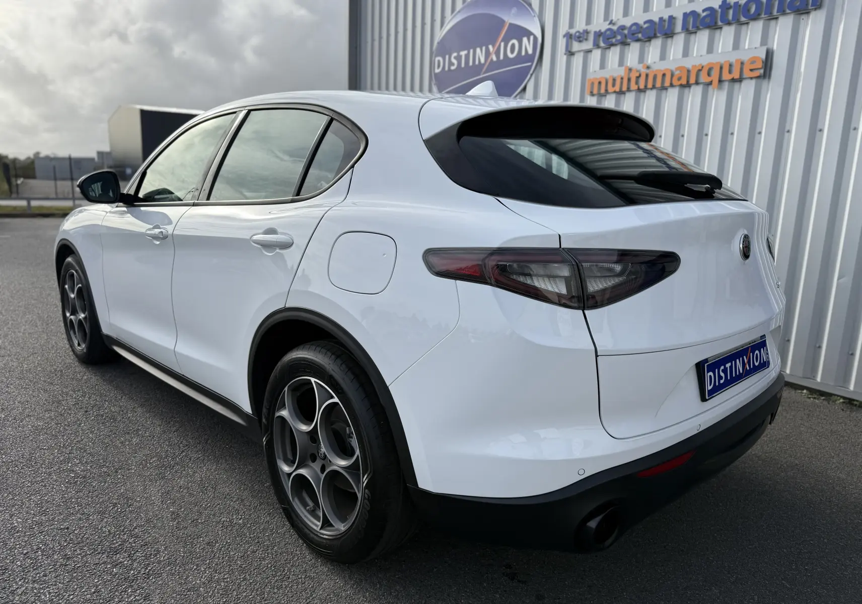 Vue 3/4 arrière droite de l'Alfa Romeo Stelvio blanc Alfa 2023 avec jantes distinctives et feux arrière foncés.