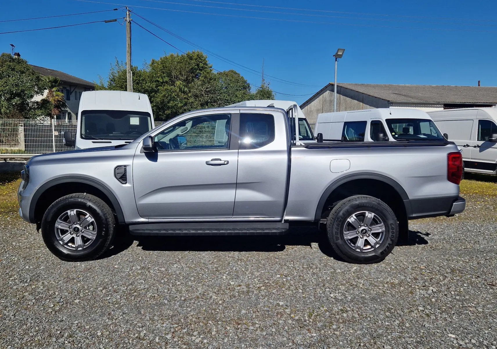 Vue de profil côté gauche d'un Ford Ranger Super Cabine gris iconic avec roues alliage et barre de protection arrière.