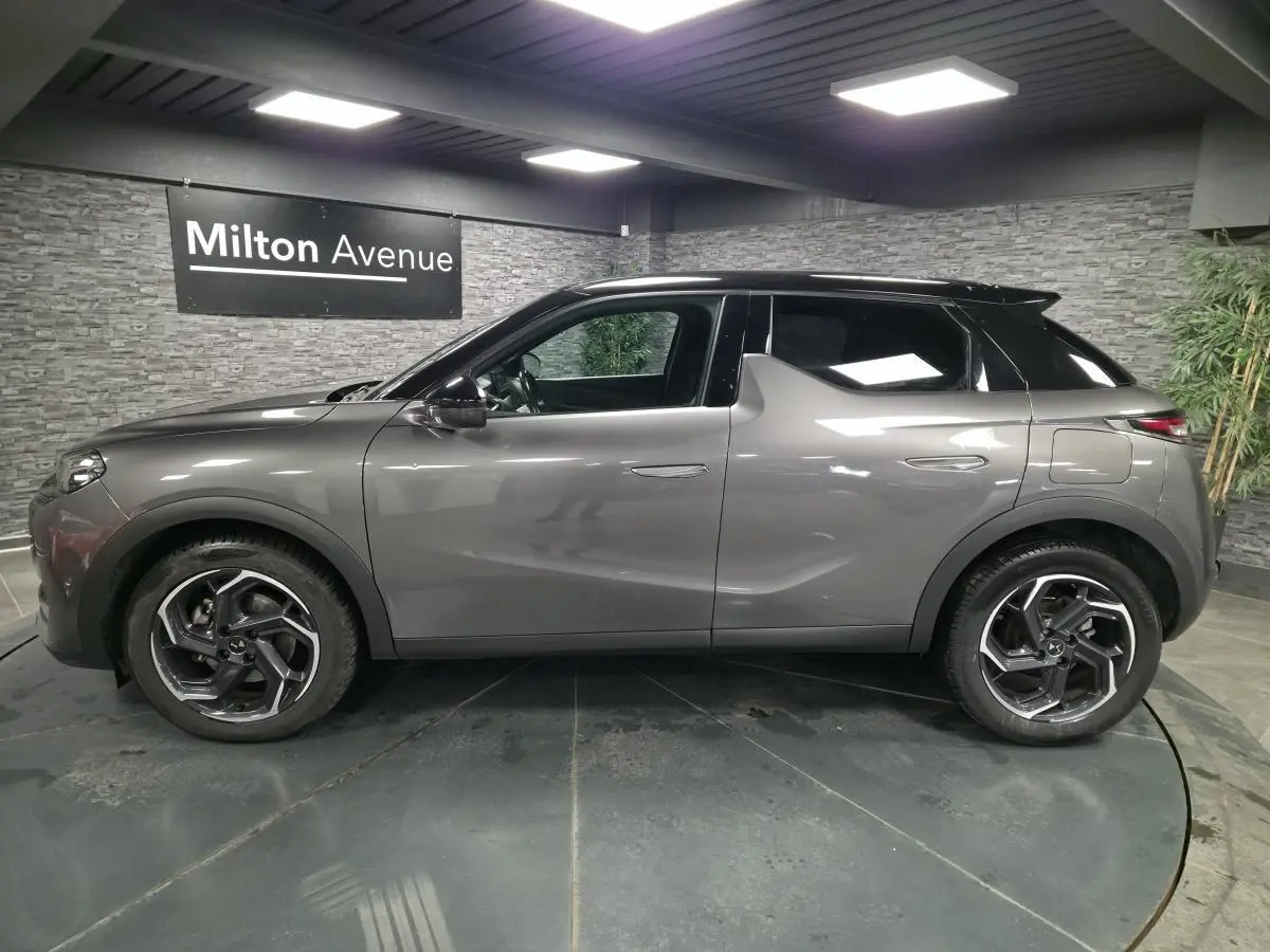 Vue de profil côté gauche du DS3 Crossback gris métallisé avec toit noir et jantes alliage 18 pouces dans un showroom.
