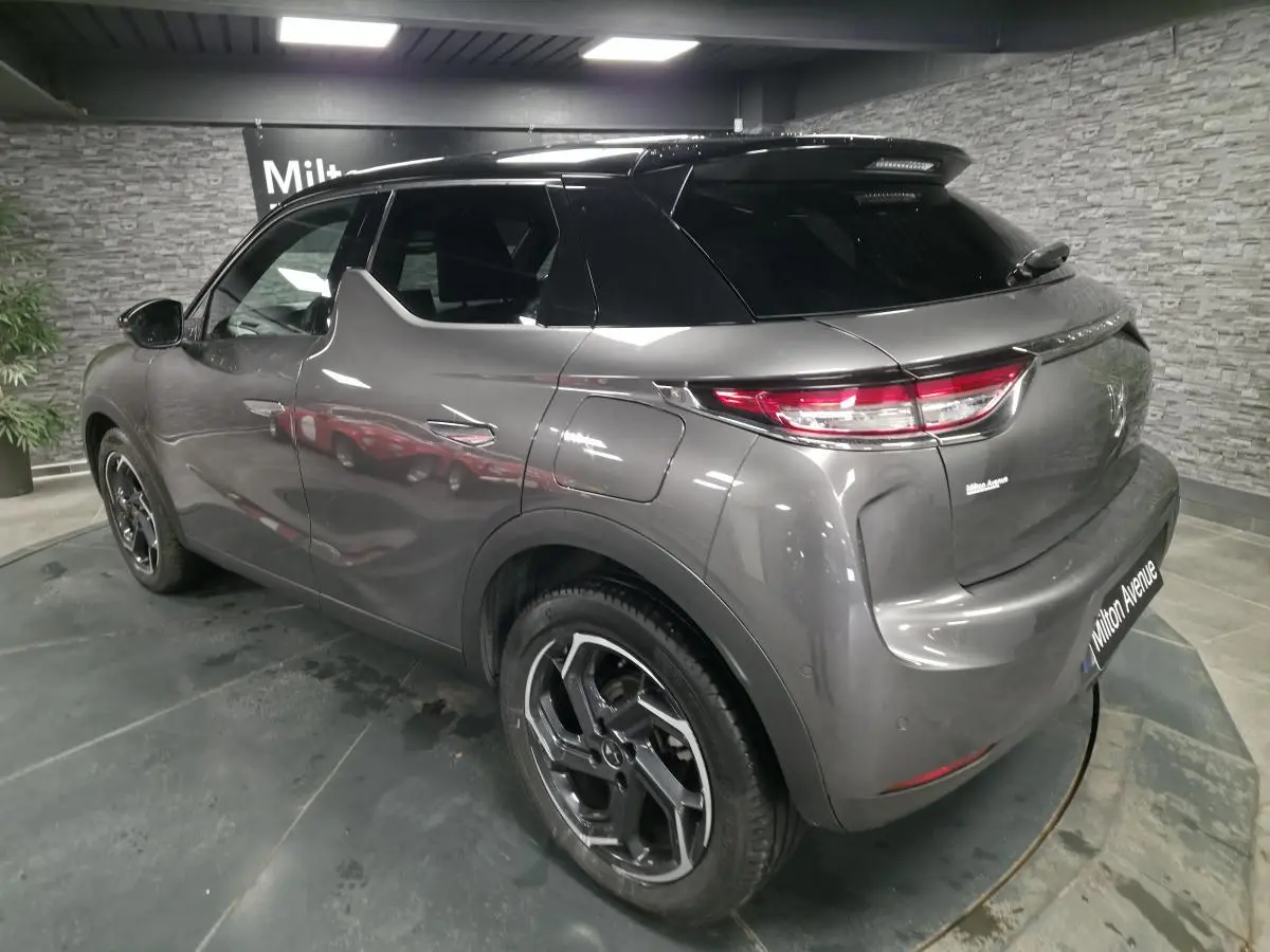 Vue 3/4 arrière droite du DS3 Crossback gris métallisé avec toit noir et jantes alliage 18 pouces en intérieur showroom.