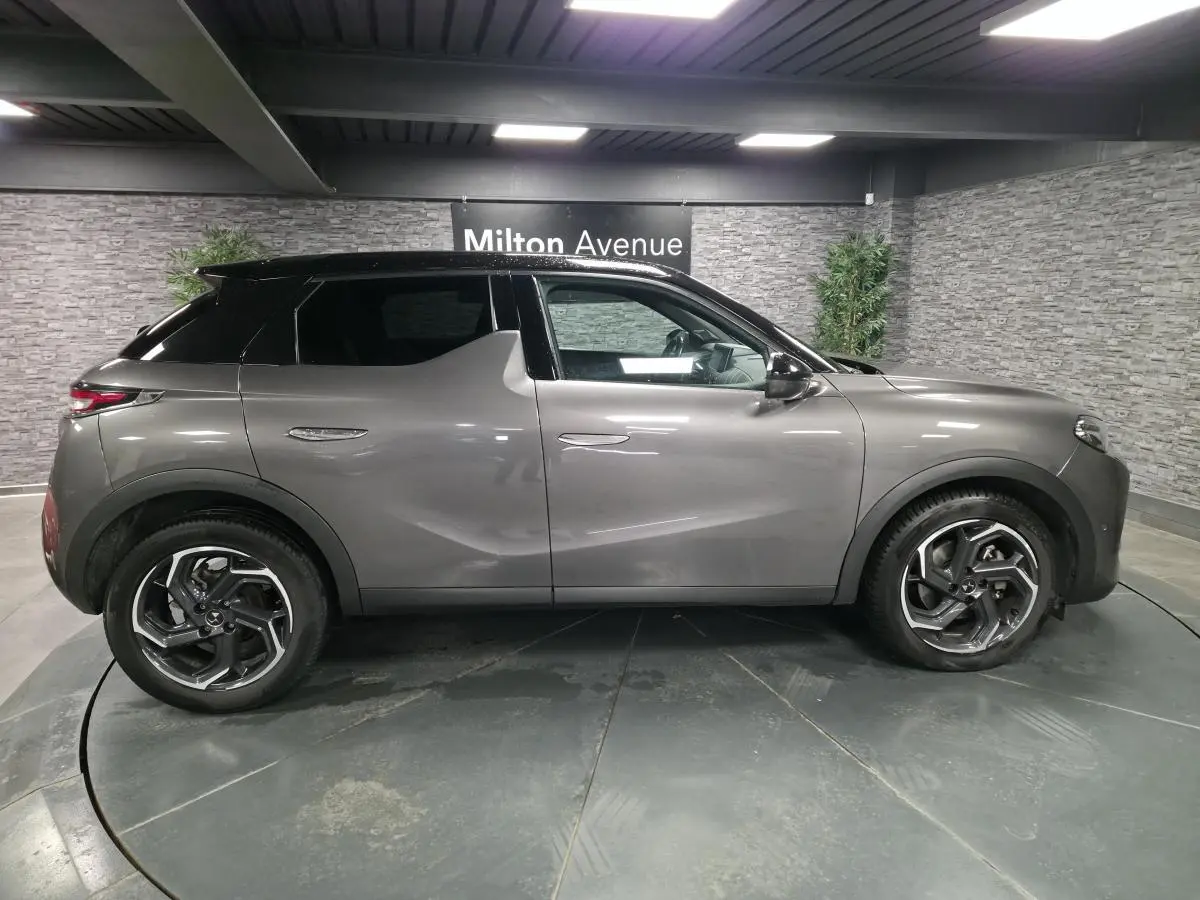 Vue latérale droite d'un DS3 Crossback gris métallisé avec toit noir et jantes alliage 18 pouces dans un showroom.