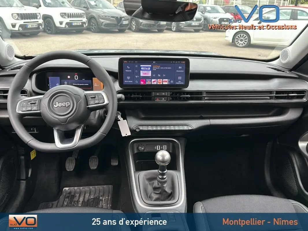 Intérieur du Jeep Avenger 2024 gris foncé, vue frontale sur le tableau de bord avec écran tactile et boîte manuelle.