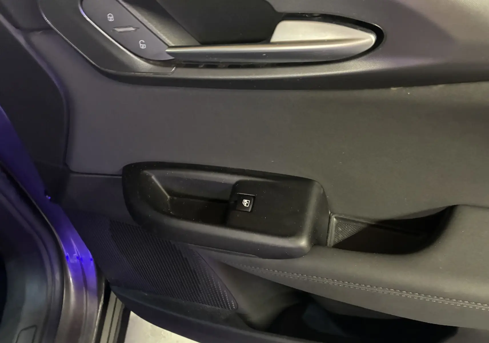 Détail de la porte intérieure côté conducteur de l'Alfa Romeo Tonale 1.3 PHEV gris foncé avec commande de verrouillage et poignée argentée.