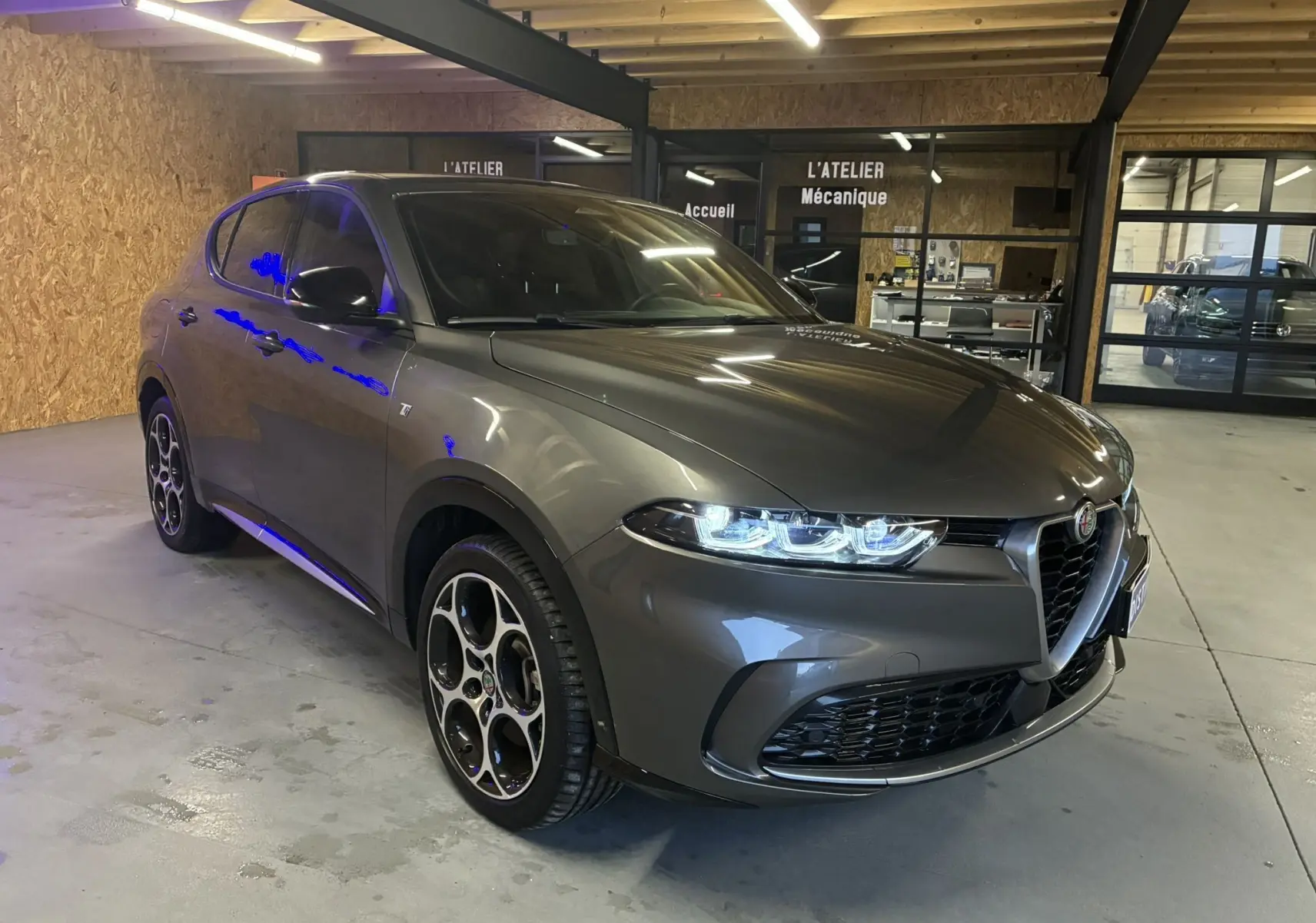 Vue 3/4 avant droit d'une Alfa Romeo Tonale gris foncé avec phares LED allumés dans un garage.