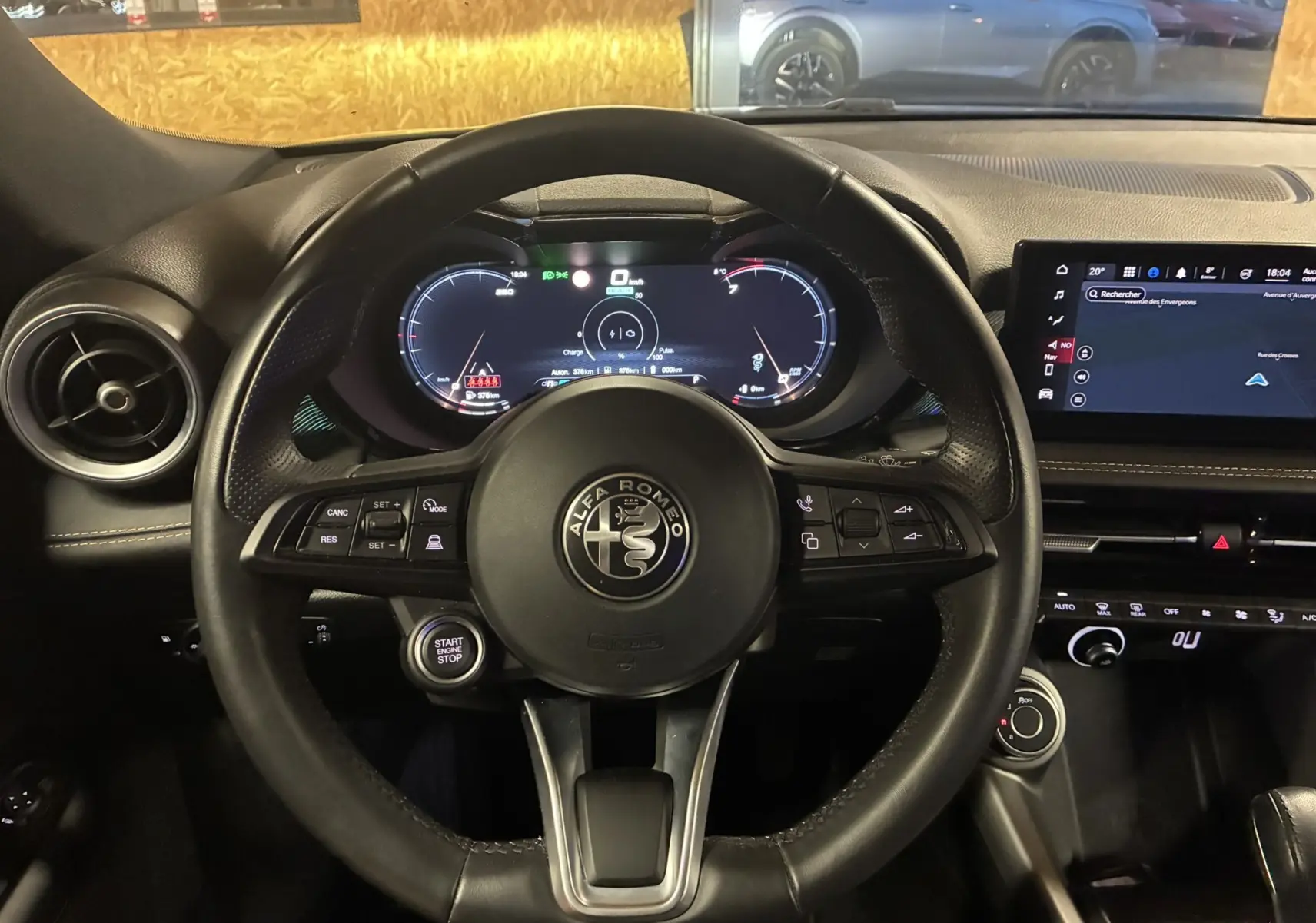 Vue intérieure centrée sur le volant noir d’un Alfa Romeo Tonale gris foncé, avec tableau de bord digital et écran tactile.