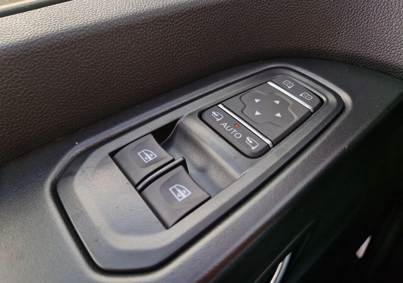 Gros plan sur les commandes de lève-vitres et réglage des rétroviseurs côté conducteur du Nissan Primastar blanc.