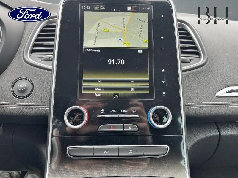 Vue rapprochée de la console centrale noire brillante du Renault Scénic blanc nacré 2022 avec écran tactile et commandes climatisation.