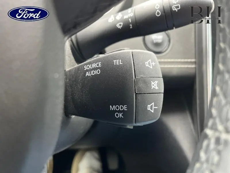 Gros plan sur la commande audio au volant noir dans l'habitacle d'un Renault Scénic blanc nacré 2022.