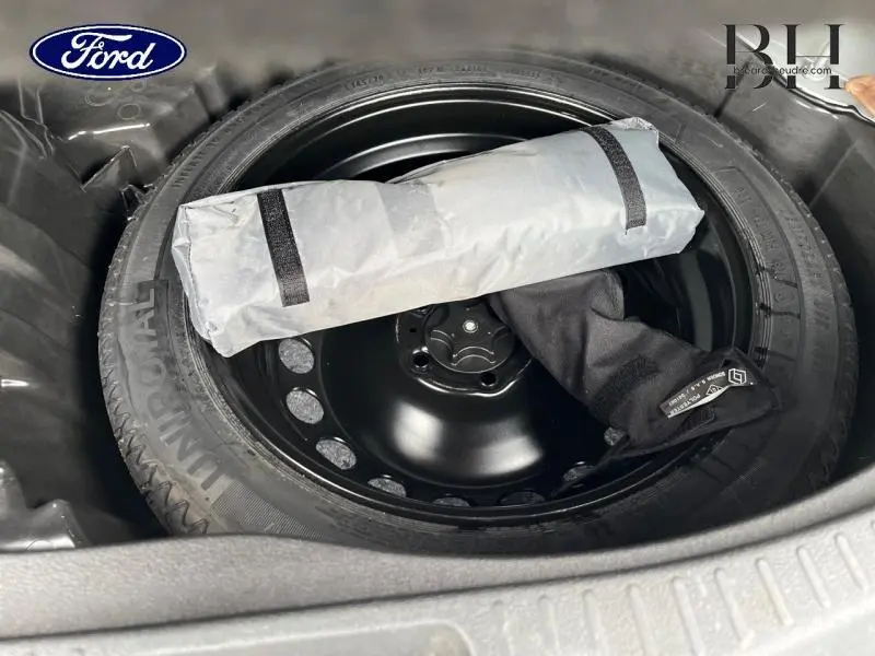 Vue plongeante sur la roue de secours galette noire dans le coffre d'une Renault Scenic blanc nacré 2022.