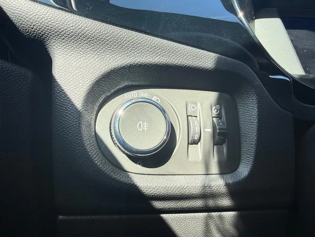 Gros plan sur la commande des phares et réglages d’éclairage dans l’habitacle noir de l’Opel Corsa rouge 2025.