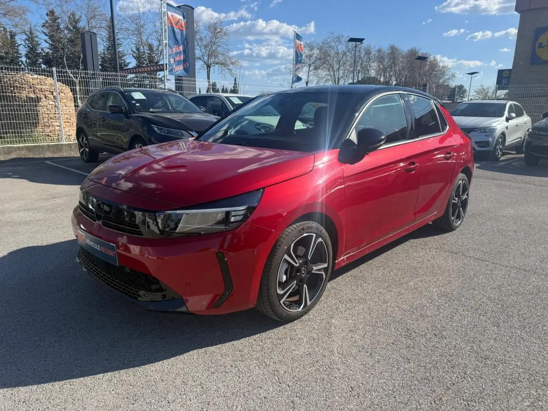 Opel Corsa rouge vue 3/4 avant droit, toit noir, jantes alliage noires et détails modernes sur calandre.