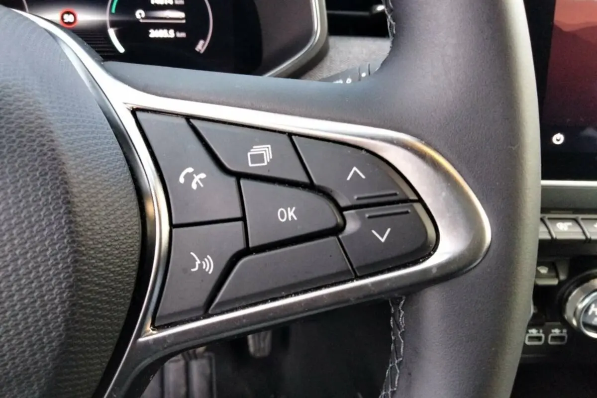 Gros plan sur les commandes multifonctions à droite du volant cuir de la Renault Clio gris rafale, tableau de bord numérique en arrière-plan.