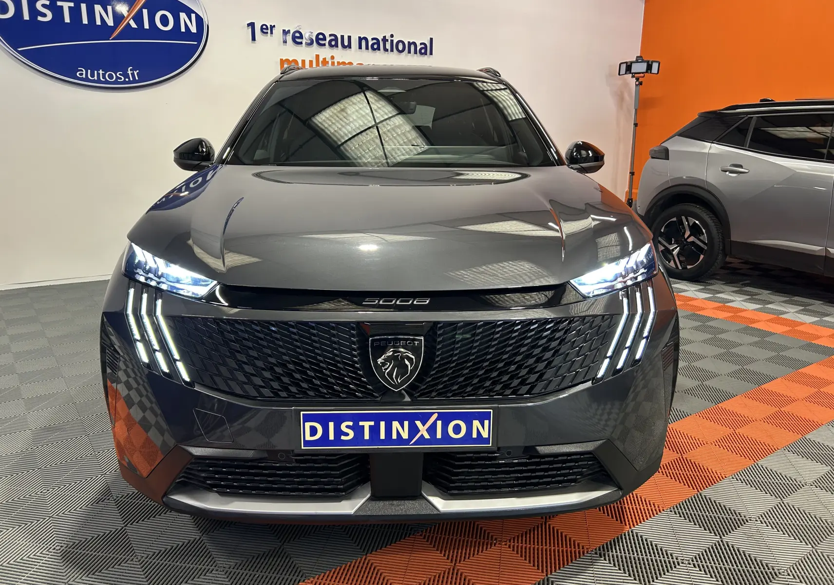 Vue de face du Peugeot 5008 Hybrid gris titane avec phares LED allumés et calandre noire texturée.