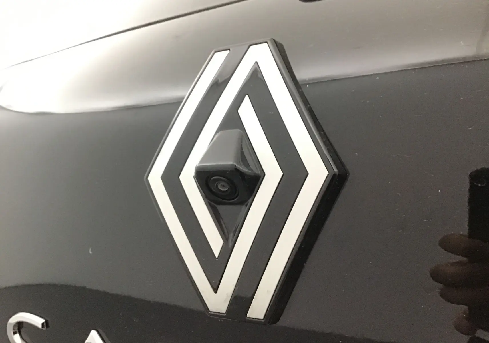 Gros plan sur le logo Renault noir et gris perle avec caméra de recul intégrée sur une Renault Captur 2025.