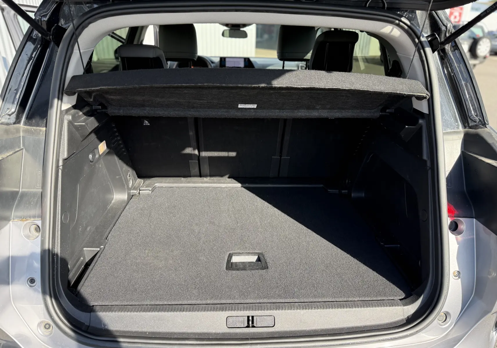 Coffre ouvert vu de l'arrière d'un Citroën C5 Aircross 2024 gris Artense avec cache-bagages relevé.