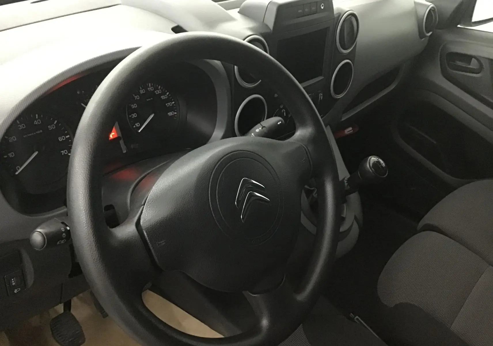 Vue intérieure côté conducteur du Citroën Berlingo blanc 2018, volant, tableau de bord et levier de vitesses manuelle visibles.