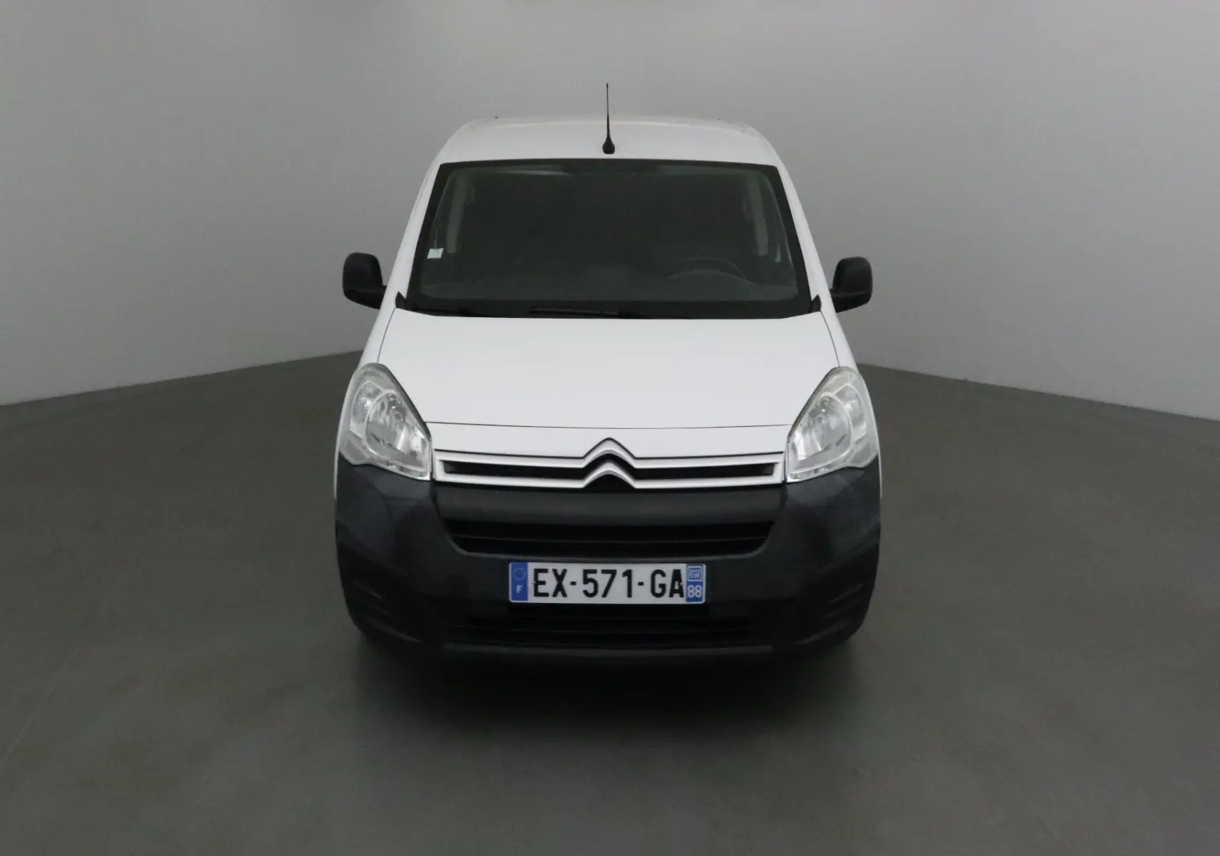 Citroën Berlingo blanc vue de face avec pare-chocs noir et calandre à chevrons argentés dans un studio gris.