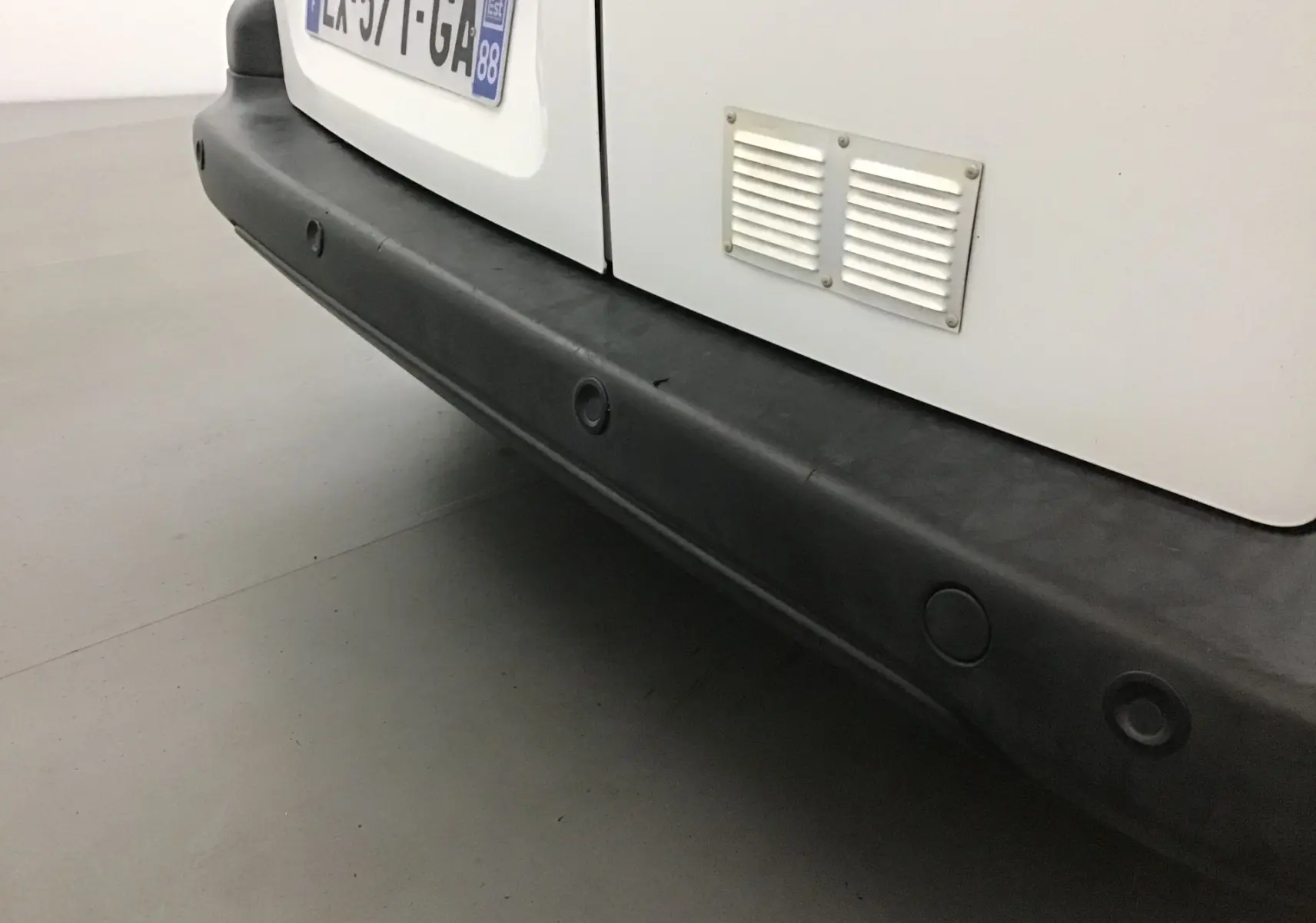 Gros plan sur le pare-chocs arrière noir du Citroën Berlingo blanc, avec la plaque d'immatriculation visible en partie.