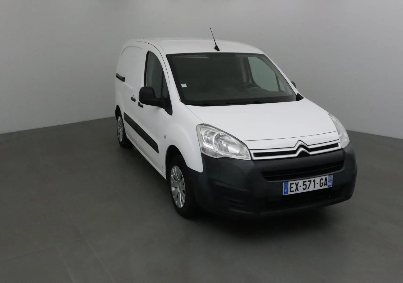 Vue 3/4 avant d'un utilitaire Citroën Berlingo blanc avec pare-chocs noir et plaques françaises visibles.