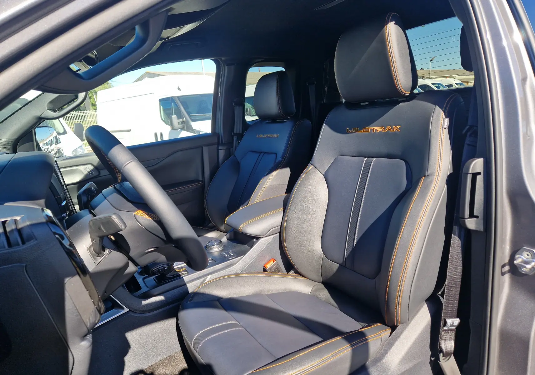 Vue intérieure côté conducteur du Ford Ranger Super Cabine Wildtrak 2026, sièges cuir gris carbone avec surpiqûres orange et logo Wildtrak brodé.