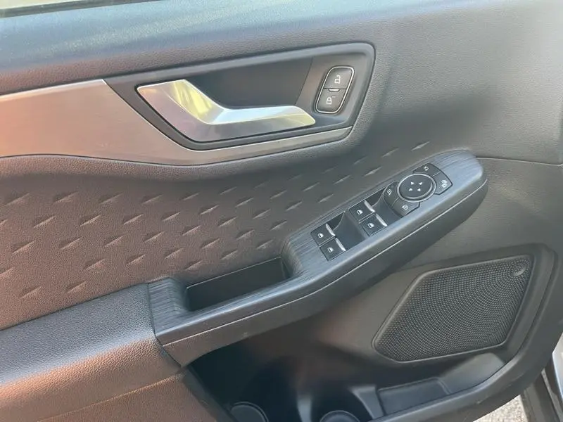 Gros plan sur la porte avant gauche du Ford Kuga gris, montrant les commandes des vitres, la poignée argentée et l'habillage texturé noir.