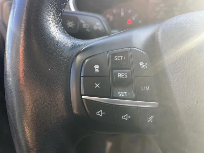 Gros plan sur les commandes de régulateur de vitesse et volume sur le volant cuir noir du Ford Kuga gris 2021.