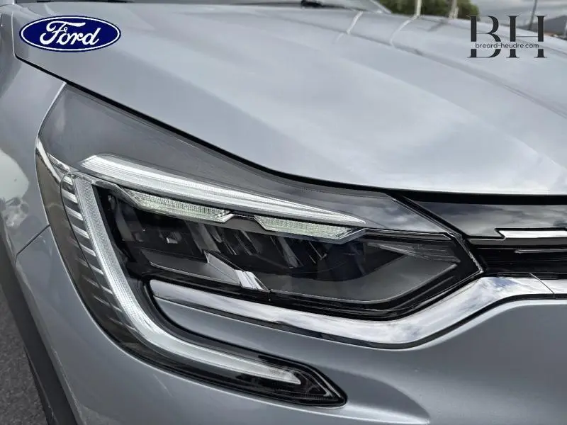 Gros plan sur le phare avant droit du Renault Captur gris Highland 2023, soulignant ses LED modernes et détails chromés.