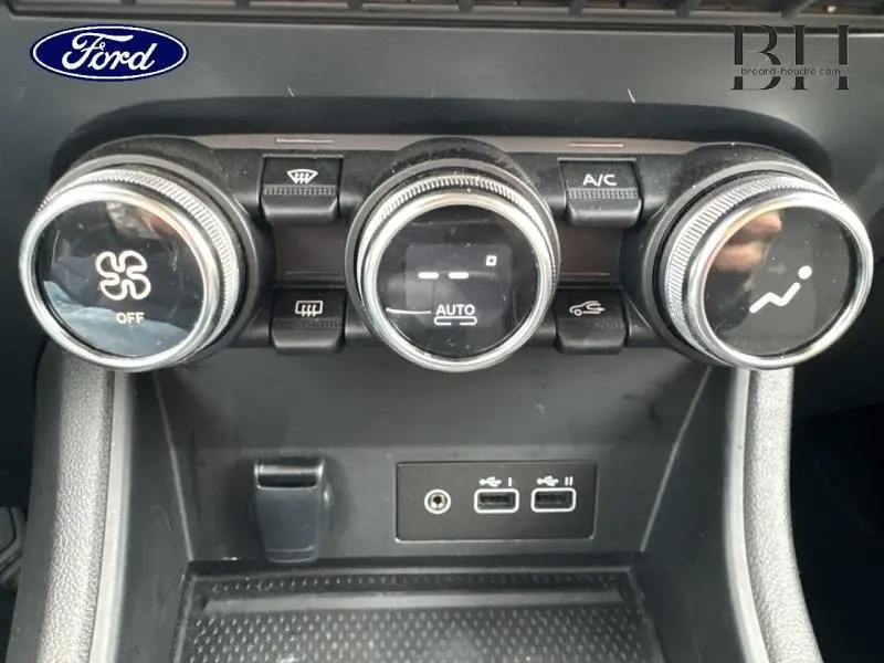 Panneau de commande de climatisation avec trois boutons rotatifs et ports USB, intérieur noir, vue de face rapprochée.