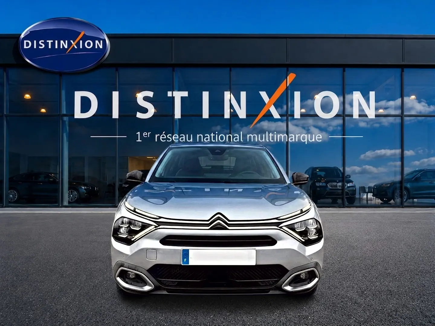 Vue frontale d'une Citroën C4 gris métallisé 2024 avec phares LED et calandre distinctive, devant un showroom Distinxion.